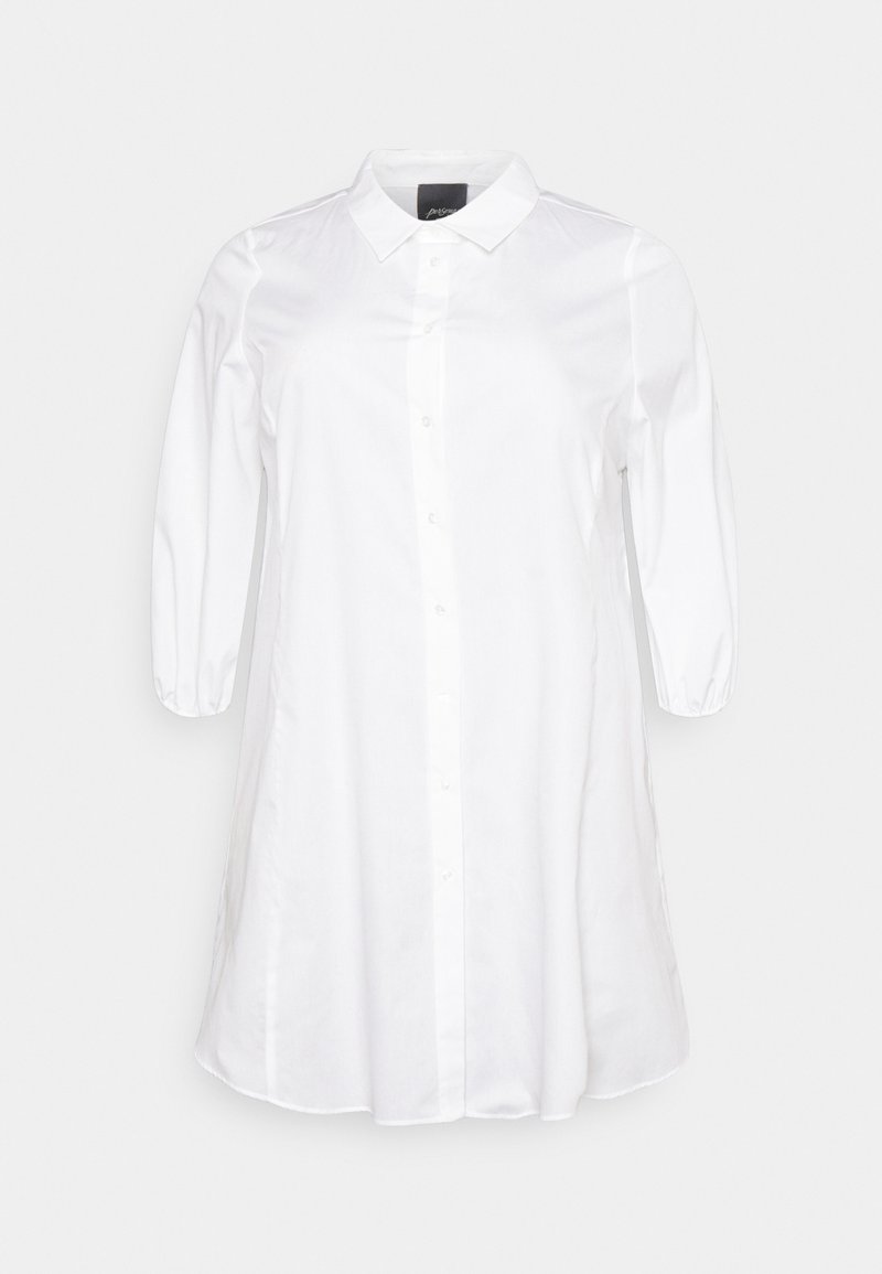 Valkoinen napilla varustettu paita, jossa on klassinen kaulus, kolmanneksi puolipitkät hihat ja hieman väljä istuvuus. Tasainen, kudottu kangas, jossa on hieno kiilto.