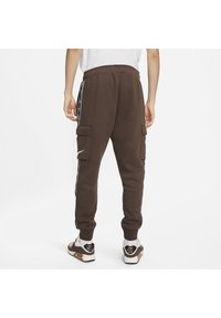 Bruna sweatpants med elastisk midja, sidostrimma och cargofickor. Kombineras med vita och bruna sneakers. Enkel vit skjorta syns ovan.