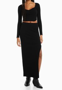 Zwart geribd twee-delig outfit met een lange mouw crop top met een ronde hals en een maxi rok met hoge split, gecombineerd met enkellaarsjes.