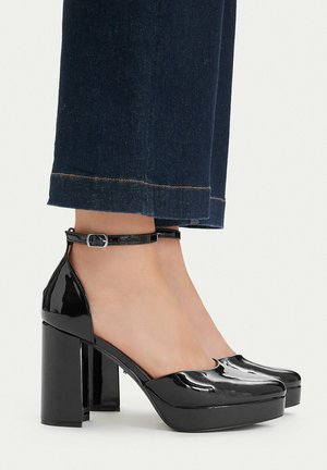 Zwarte plateauhakken van lakleer met enkelbandjes, gedragen met donkerblauwe cropped jeans.
