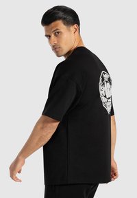 Camiseta de algodón negra, de corte oversized, con un diseño gráfico blanco en la parte posterior que parece una cara. Manga corta y cuello redondo.