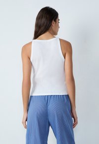 Top bianco senza maniche con scollatura rotonda e design aderente, abbinato a pantaloni larghi a righe blu; texture del tessuto minimalista.