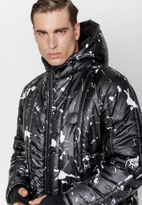 Kurtka puchowa w kolorze czarnym z białym wzorem w plamy. Posiada kaptur, zamek błyskawiczny oraz elastyczne mankiety. Wykonana z błyszczącego, ocieplanego materiału.