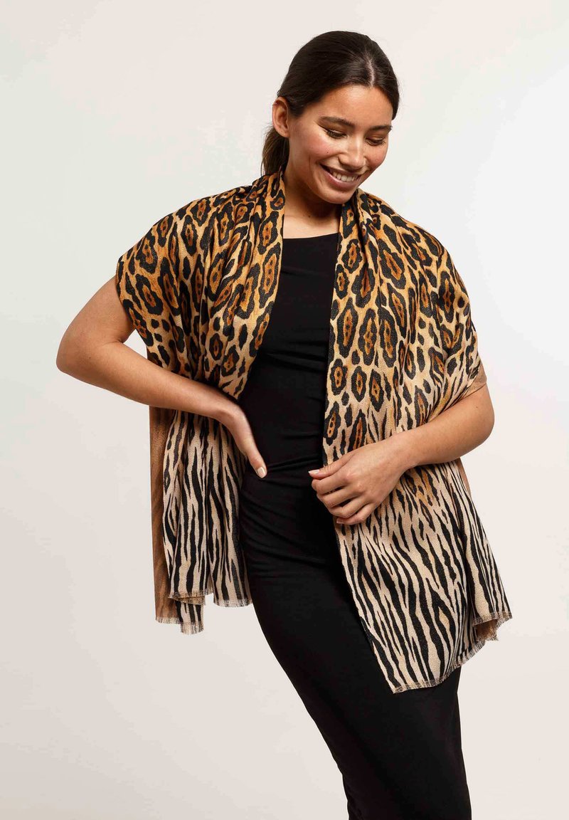 Lightweight scarf featuring a bold animal print with tan and black stripes, finished with fringed edges. Draped over a black outfit.