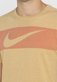 Primer plano de una persona que lleva una camiseta beige con un gran logotipo del swoosh de Nike en color naranja en el pecho.