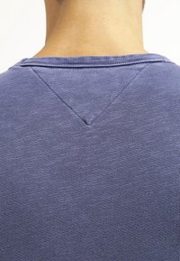 Námořnicky modrý svetr s ribkovaným vzorem, který má na zadní straně detaily ve tvaru V. Tkanina vypadá jemně s jemnou strukturou a subtilními barevnými variacemi.