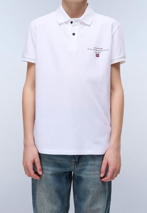 Osoba ubrana w biały, krótkim rękawem polo z dwoma czarnymi guzikami oraz małym czarnym napisem i logo norweskiej flagi na lewej piersi.