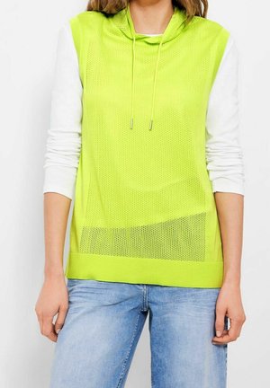 Felpa a rete gialla neon con cappuccio regolabile, indossata sopra una maglietta a maniche lunghe bianca, caratterizzata da un orlo a costine e una vestibilità casual.