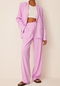 Jasnofioletowa marynarka z dopasowanymi spodniami o szerokich nogawkach; gładki materiał, dopasowany krój, zapięcie na jeden guzik i detal kieszeni z przodu.