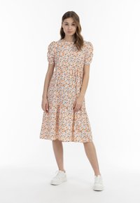 Blumiges Midikleid mit Puffärmeln, orange und blaue Muster auf wei�ßem Stoff, gestufter Rock, getragen mit weißen Sneakers.
