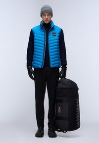 Blå pufferväst, marinblå tröja, svarta handskar, svarta byxor och svarta stövlar. Bär en stor svart duffelväska med en norsk flagga.