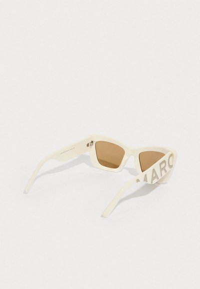 Gafas de sol rectangulares color crema con lentes marrones y el texto "MARC" en la varilla izquierda, mostradas sobre un fondo blanco.