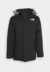 Parka noire isolée avec capuche doublée en fausse fourrure, fermeture éclair à l'avant et logo sur la poitrine gauche. Comprend des poches latérales et des poignets élastiques.