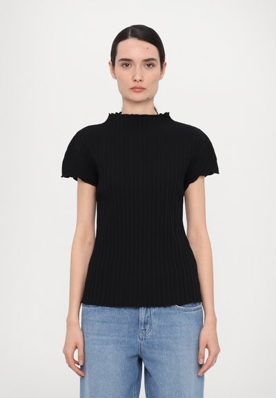 Svart ribbestrikket topp med høy volangkrage og korte ermer, kombinert med lyseblå denimjeans. Passformen er kroppsnær.