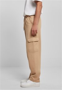 Beige cargo sweatpants med avslappnad passform, sidofickor, dragsko i midjan och ribbade mudd, parat med vita sneakers.
