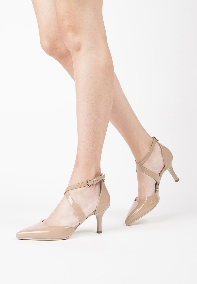 Beige patent leather heels with pointed toes, ankle strap, and 5 cm stiletto heels. Features crisscross design at the front.
