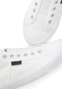 Weiße Leinensneaker mit niedrigem Design, metallischen Ösen, Gummisohle und einem schwarzen Logopatch an der Seite. Strukturelle Details auf der Sohle.