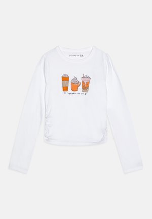 Biała bluzka z długim rękawem z ilustracjami filiżanek kawy w odcieniach pomarańczowym i brązowym, z napisem "W mojej erze dyniowego przyprawy" poniżej wzorów.