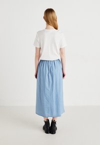 T-shirt bianco abbinato a una maxi gonna in denim blu. La gonna ha una vita elastica e arriva a metà polpaccio, abbinata a stivaletti neri.