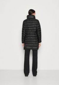 Zwarte pufferjas met een cinched taille, hoge kraag en een reliëflogo op de kraag. Gladde textuur en knielange ontwerp.