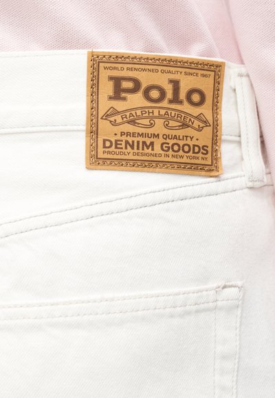 Καφέ δερμάτινο κονκάρδα Polo Ralph Lauren σε λευκό τζιν παντελόνι, φορεμένο με ανοιχτό ροζ πουκάμισο.