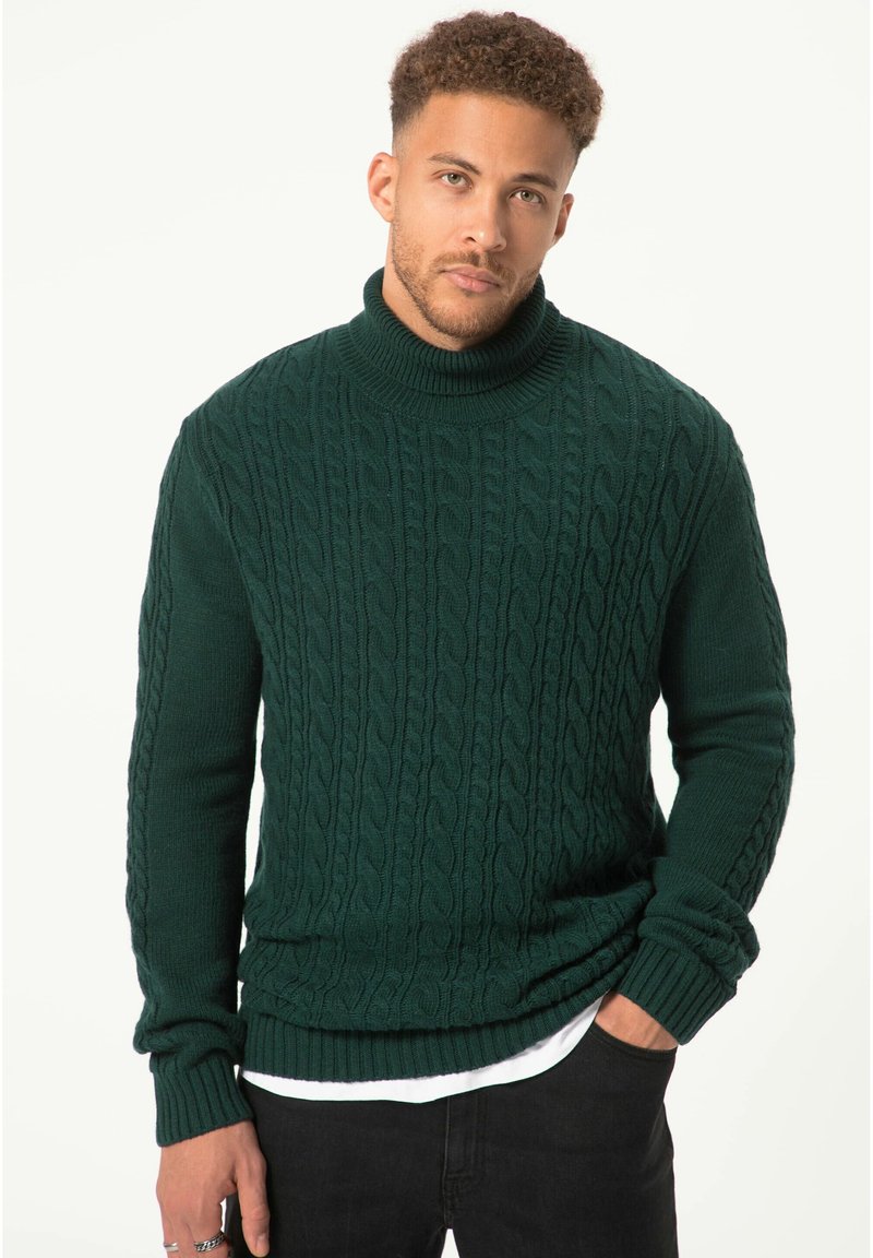 Dunkelgrüner Strickpullover mit Rollkragen, der ein Kabelstrickmuster aufweist, gerippte Bündchen und Saum hat und über einem weißen Hemd getragen wird, vor einem hellen Hintergrund.