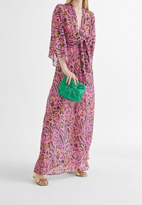 Maxiklänning i rosa med leopardmönster och gröna accenter, med djup V-ringning, breda ärmar och knytbart midjeband. Matchas med en grön kuvertväska.