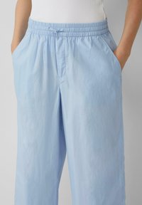 Pantalons bleu clair, amples, avec une taille élastique et un cordon de serrage. Dotés de poches latérales et d'une texture lisse, légèrement brillante.