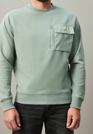 Sudadera verde claro hecha de material suave, con un bolsillo frontal con cremallera, puños acanalados y un cuello redondo.