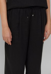 Zwarte linnenbroeken met een trekkoord in de taille, voorzien van subtiele plooien, een gladde textuur en metallic accenten op de uiteinden van het trekkoord.