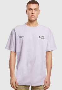 Lyse lilla bomulds T-shirt med korte ærmer. Forsiden har teksttryk: "LIFE" i fed skrift og et citat på venstre side. Løs pasform.