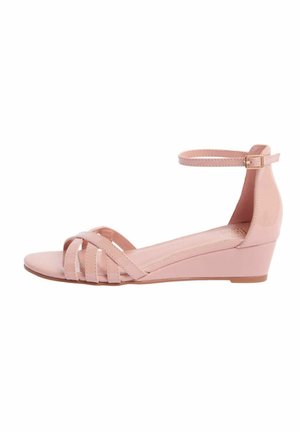 Sandale roz cu toc în formă de pană, cu vârf deschis și barete încrucișate în față, precum și o curea la gleznă cu o cataramă mică, pe fundal alb.