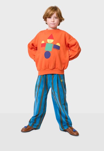 Sudadera naranja con un estampado geométrico colorido; pantalones a rayas azules y verdes; zapatos marrones con borlas azules.