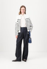 Stripet svart og hvit cardigan, hvit skjorte med knapper, vide mørk denim bukser, svarte spisse leiligheter, og en blå crossover-veske.