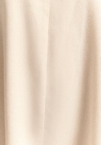 Beiger Stoff mit strukturierter Oberfläche; gewebtes Muster; wirkt weich und leicht; weist subtile Farbtonvariationen auf.