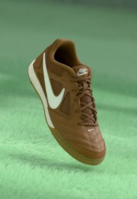 Smeđi kožni Nike tenisice s bijelim detaljima, teksturiranim gornjim dijelom i prepoznatljivim swoosh logom. Lagani dizajn s gumiranim potplatom.