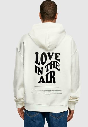 Hvid hoodie med teksten "KÆRLIGHED I LUFTEN" i fed sort skrifttype på ryggen. Fremstillet af bomuldsmateriale med en afslappet pasform og justerbar hætte.