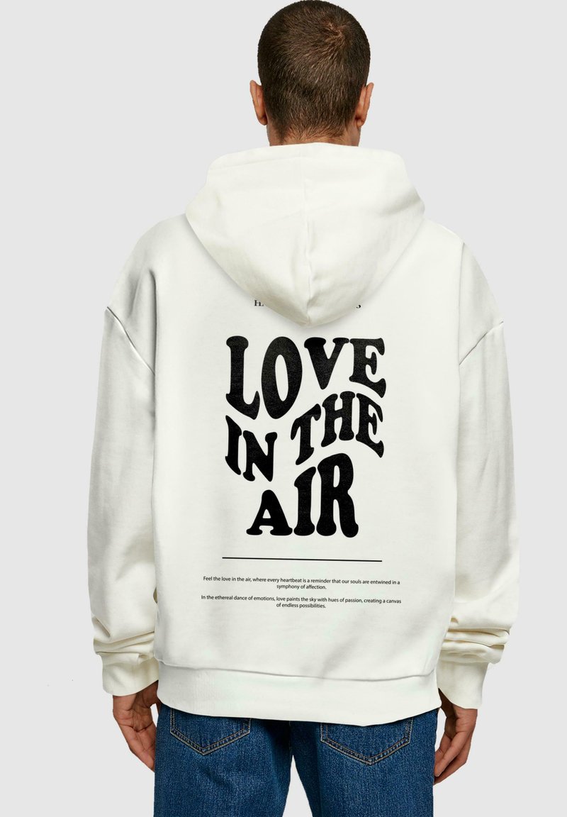 Hvid hoodie med teksten "KÆRLIGHED I LUFTEN" i fed sort skrifttype på ryggen. Fremstillet af bomuldsmateriale med en afslappet pasform og justerbar hætte.