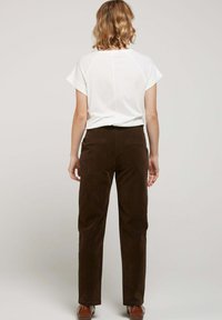 Haut blanc à manches courtes associé à un pantalon en velours côtelé marron foncé ; texture lisse, coupe droite et détails subtils sur les poches arrière.