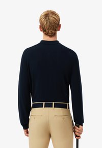 Marineblauw poloshirt met lange mouwen, met een zachte structuur en een achterste kraag, gecombineerd met lichtbeige, getailleerde broek en een zwarte riem.