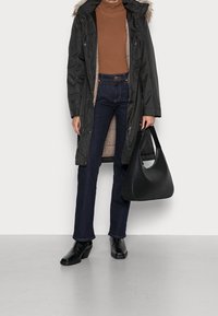 Zwarte parka met nep-bonten trim, bruine geribde coltrui, donkerblauwe flared jeans en zwarte haklaarzen. Zwarte hobo tas met gebogen handvat.