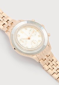 Ροζ χρυσό ρολόι χειρός με στεφάνι από στρας, λευκό καντράν, τρεις υποκαντράν και μεταλλικό μπρασελέ με συνδέσμους σε ανοιχτό φόντο.