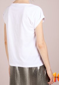 Camisa blanca de manga corta con puños enrollados, combinada con una falda plisada plateada metálica. Diseño simple y limpio con una textura suave.