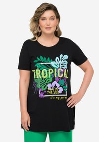 Černé bavlněné tričko s krátkým rukávem, zdobené tropickou grafikou s zelenými listy, fialovými květinami a žlutým nápisem "TROPICKÁ ZÁBAVA NA SLUNCI."
