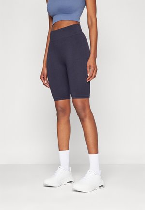 Frau trägt marineblaue, gerippte Biker-Shorts mit hoher Taille, hellblaues kurzes Tanktop, weiße Knöchelsocken und weiße Sportschuhe.