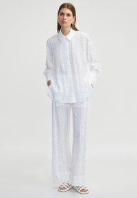 Wit gestreepte outfit met een knoopshirt en bijpassende wijde broek, beide met rijen delicate zilveren versieringen.