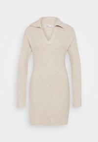 Stickad klänning i ljusbeige med V-ringning och krage. Har långa ärmar och ribbat mönster för extra detalj.
