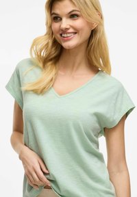 Jasnozielona koszulka z dekoltem w serek i krótkimi rękawami, wykonana z miękkiego materiału z delikatną teksturą. Luźny i swobodny krój.