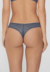 Dunkelblaue Spitzen-Tanga mit gewelltem Bund und floralem Muster. Eng an den Körper anliegend, mit einem minimalistischen Rückenteil.