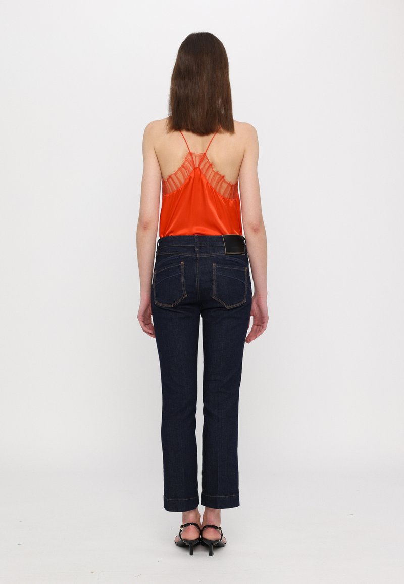 Red satin top with lace detailing at the back, paired with dark blue denim jeans and black strappy heels. Minimalist design, fitted style.